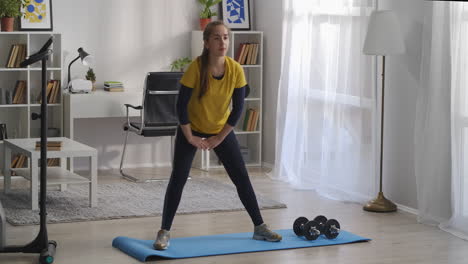 sporty-teenager-girl-is-doing-exercises-for-legs-in-living-room-squatting-on-sides-and-tensing-muscles-of-hips-helathy-lifestyle-and-sport-activities